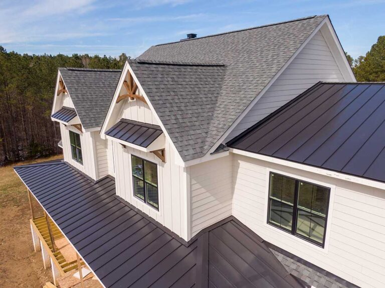 A residential roof with solar panels, reflective shingles, and a small planted section beside a snowy yard