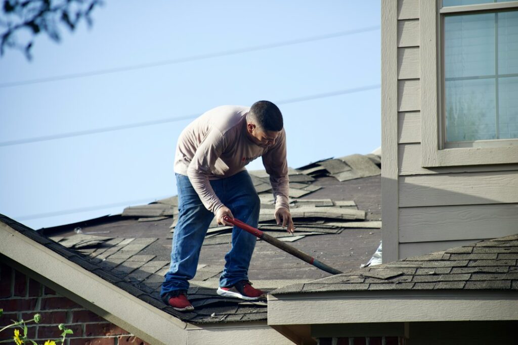 Homeowner and roofing contractor reviewing shingles, flashing, and a written project estimate beside a house.